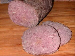 Sliced homemade summer sausage on a wooden cutting board, ready to serve with crackers or cheese.