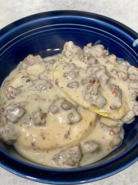 Southern sausage gravy poured over biscuits in a blue bowl, creamy and peppered.