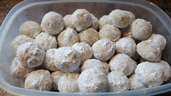 Batch of Mexican wedding cake cookies coated with powdered sugar in a plastic storage containe