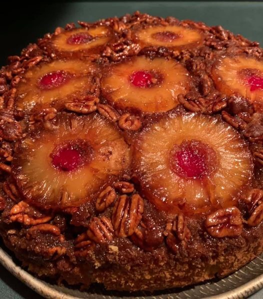 A freshly baked Upside-Down Candied Pecan Pineapple Cake served on a round tray, displaying a glossy topping of caramelized pineapple rings, cherries, and glazed pecans.