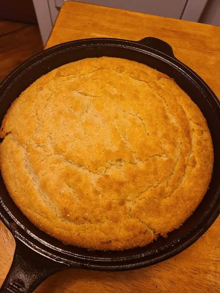A golden brown, perfectly baked round cornbread resting on a plate.