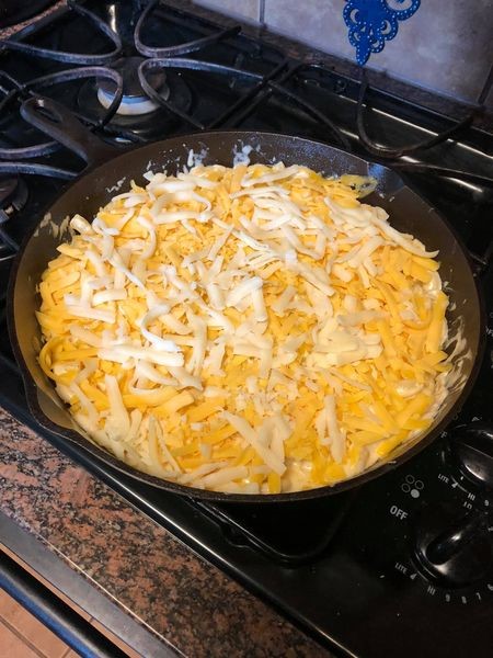 Unbaked Chicken and Cheese Macaroni Bake topped with shredded mozzarella and cheddar cheeses in a cast iron skillet ready for the oven