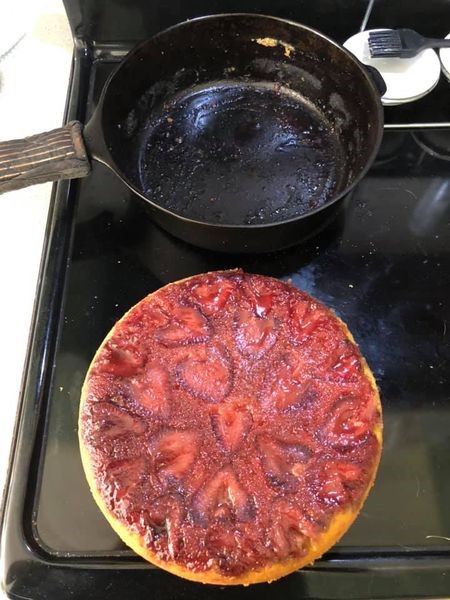 Fresh strawberry halves arranged tightly in a heart-like pattern inside a cast iron skillet with melted butter and sugar.