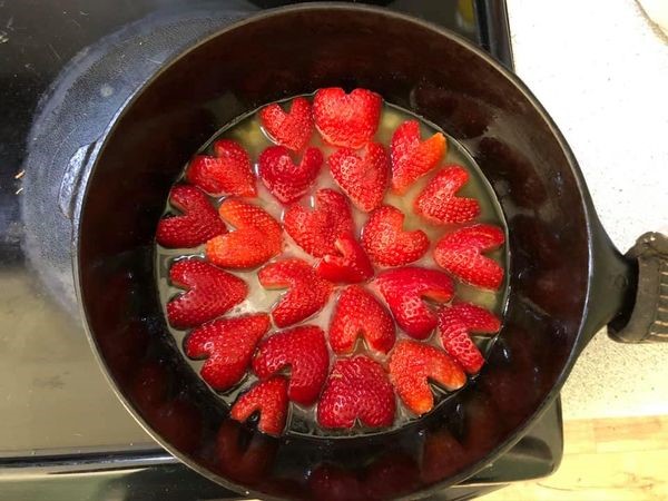 Fresh strawberry halves arranged tightly in a heart-like pattern inside a cast iron skillet with melted butter and sugar.