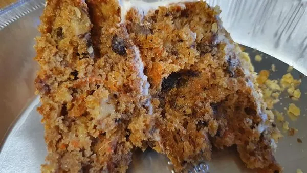 A slice of carrot cake showing shredded carrots, pineapple, and raisins; cream cheese frosting on carrot cake.