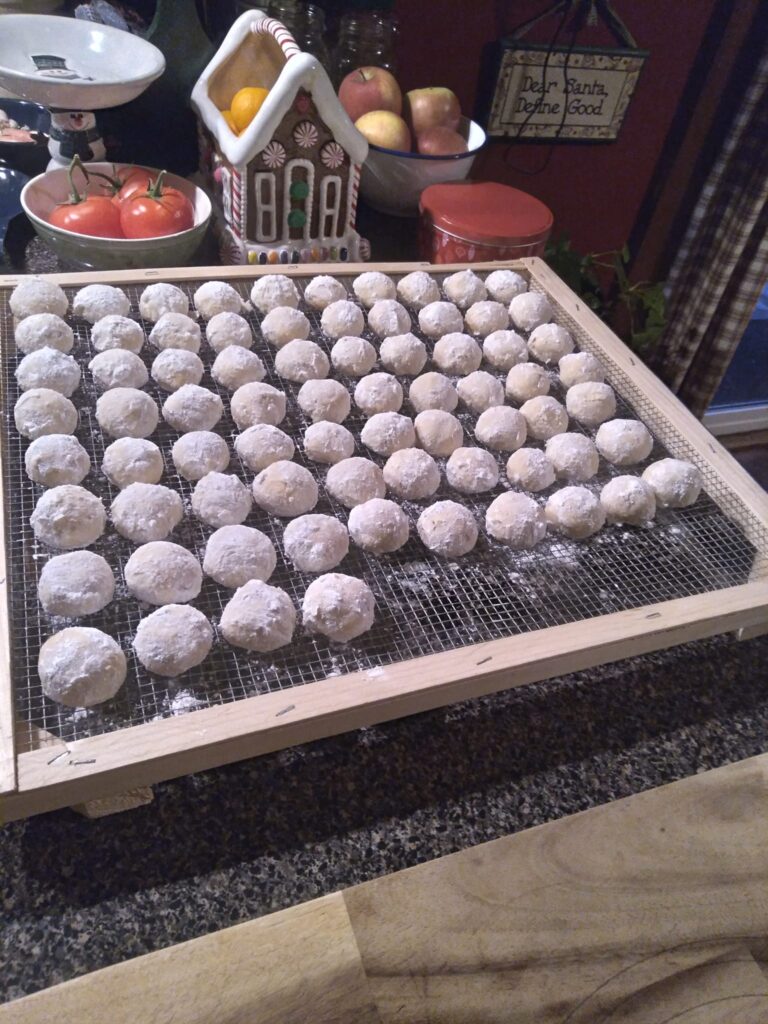 A tray of Russian Tea Cakes rolled in powdered sugar, cooling on a rack in a festive kitchen