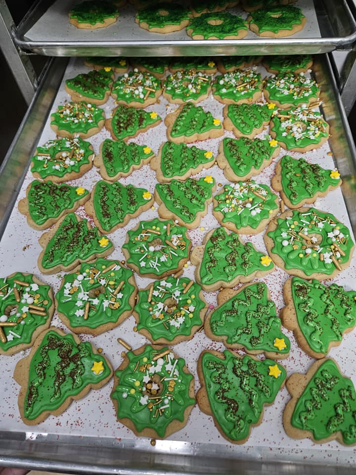 A tray of green Christmas tree sugar cookies with festive decorations.