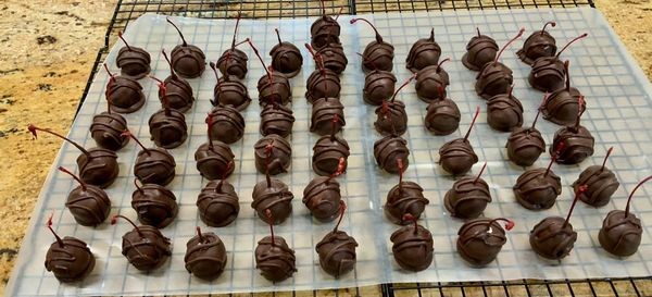 Rows of finished chocolate cherry cordials with shiny chocolate shells, cooling on a rack – classic liquid center cherry cordials