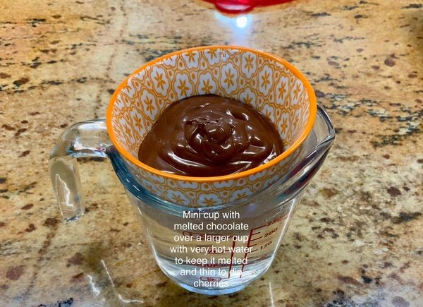 Mini cup of melted chocolate over a cup of hot water to keep it thin and melted for dipping cherries – homemade cherry cordials tip