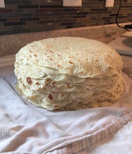 A stack of soft, golden-brown lefse made from Grandma’s recipe, cooling on a dish towel in the kitchen