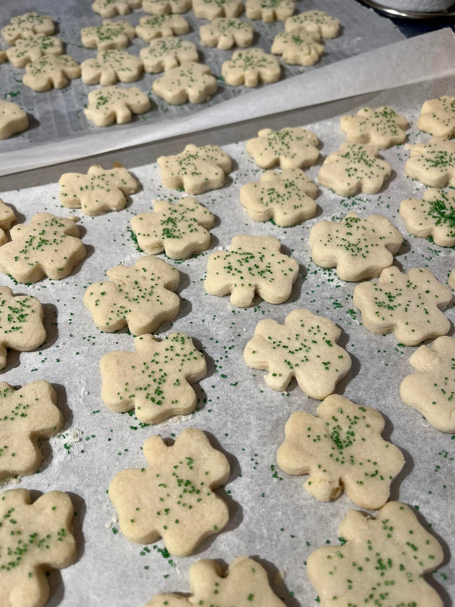 Shamrock-shaped shortbread cookies on a baking sheet, sprinkled with green sugar