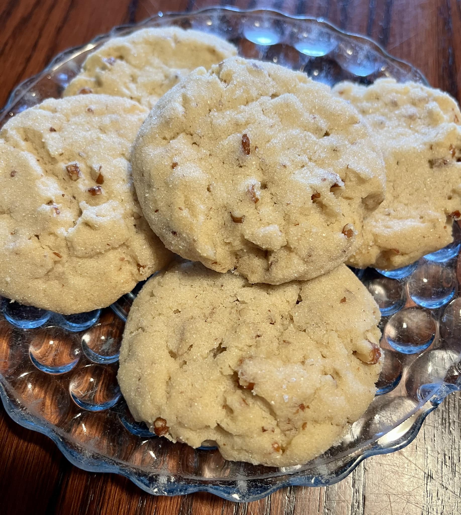 A plate of homemade pecan sandies, featuring buttery cookies with chopped pecans, dusted with sugar