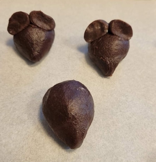 Three raw chocolate mouse-shaped cookie dough pieces with ears, sitting on parchment paper