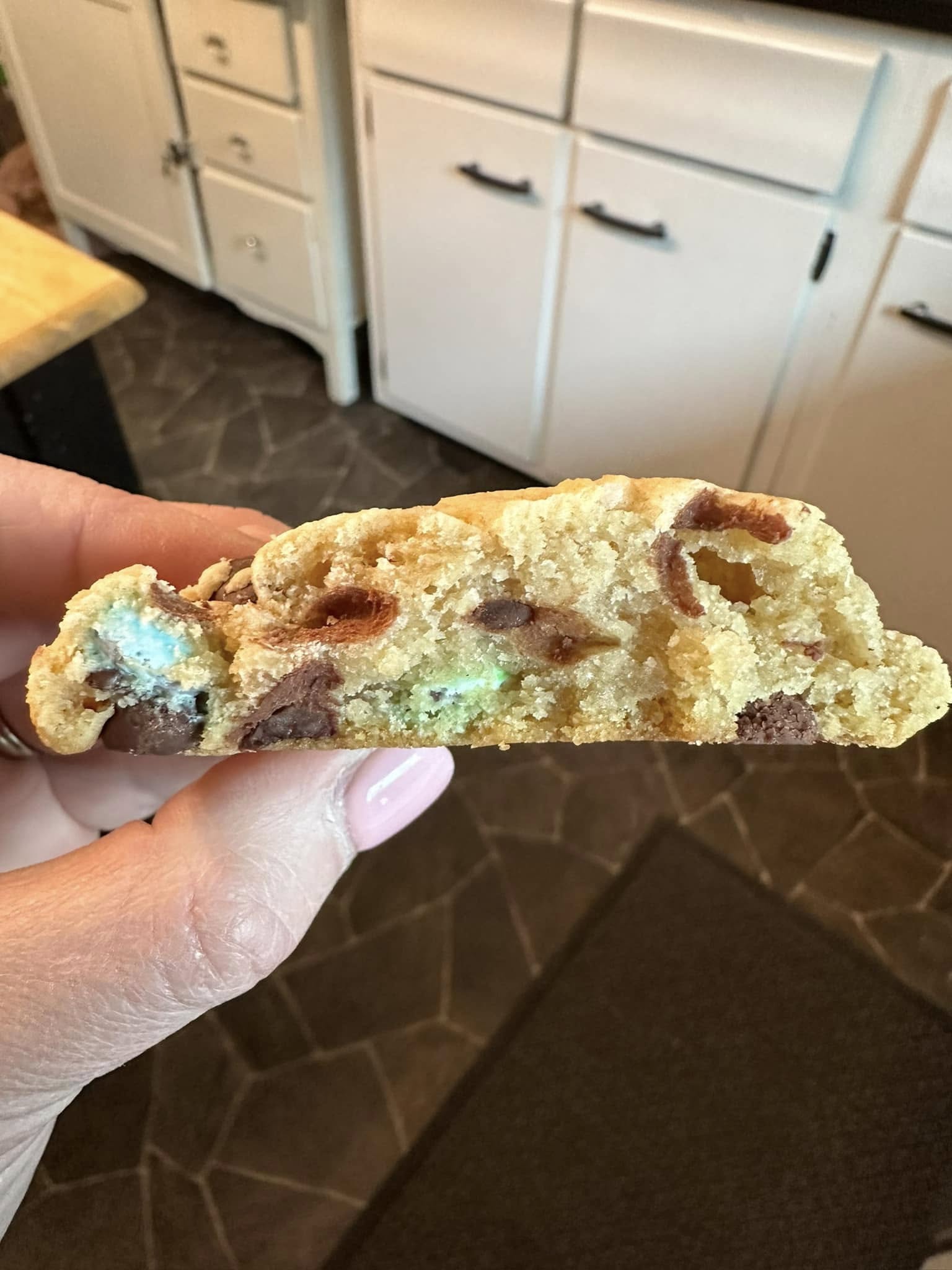 A thick, soft M&M chocolate chip cookie broken in half, revealing a gooey center