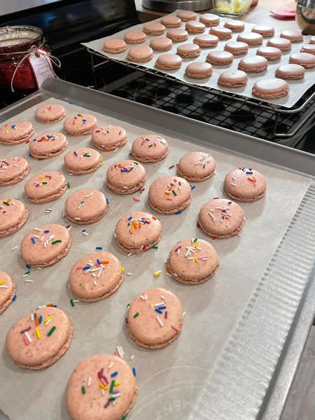 A single pink macaron filled with cotton candy buttercream frosting, topped with a swirl and rainbow sprinkles