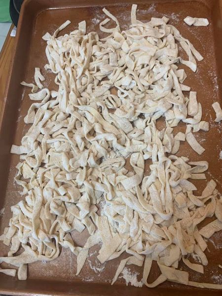 Freshly rolled and cut homemade egg noodles, lightly dusted with flour, resting on a baking tray."