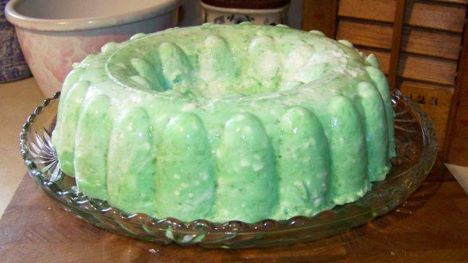 A vibrant green Jello salad in a bundt mold on a glass serving plate."