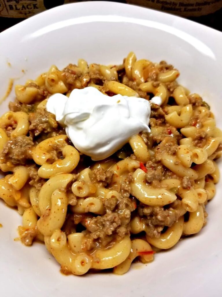 A bowl of queso blanco goulash with elbow macaroni, taco-seasoned meat, and sour cream on top.