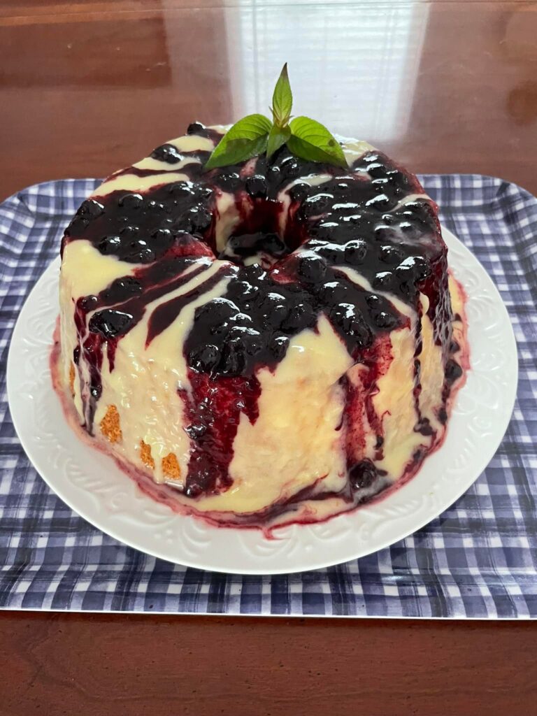 A full view of the Angel Food Cake topped with lemon curd and blueberry compote, garnished with a mint leaf.
