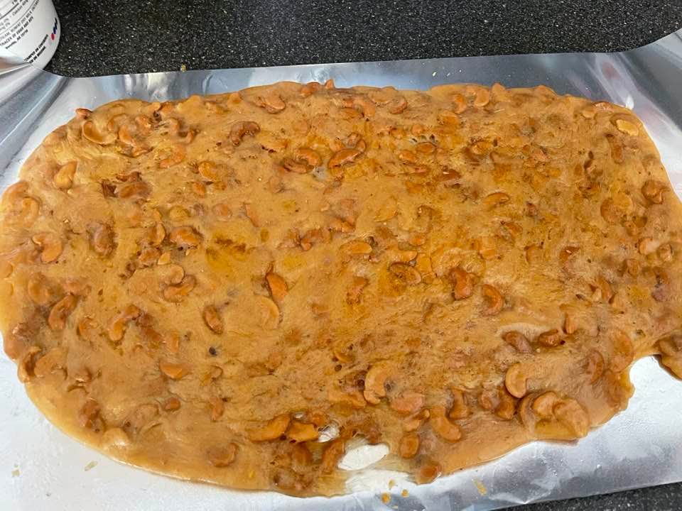 Freshly made cashew brittle cooling on a greased cookie sheet, filled with golden caramelized cashews.