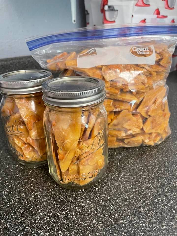 Homemade microwave cashew brittle stored in mason jars and a ziplock bag, ready for gifting