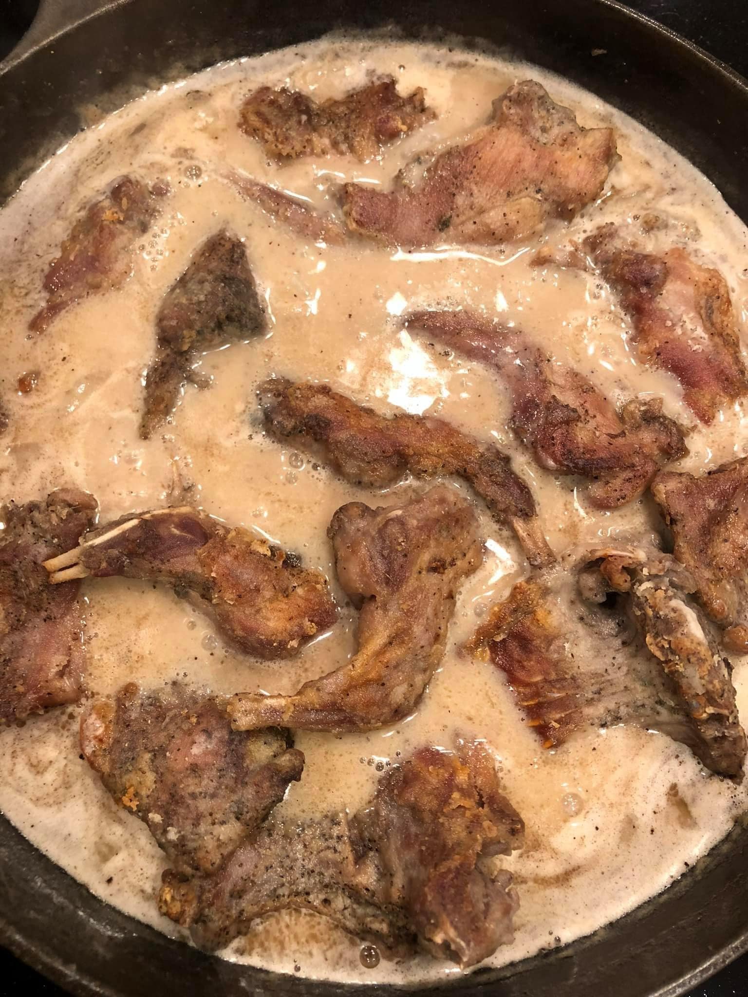 Golden-brown fried squirrel pieces simmering in creamy pepper gravy, ready to be baked