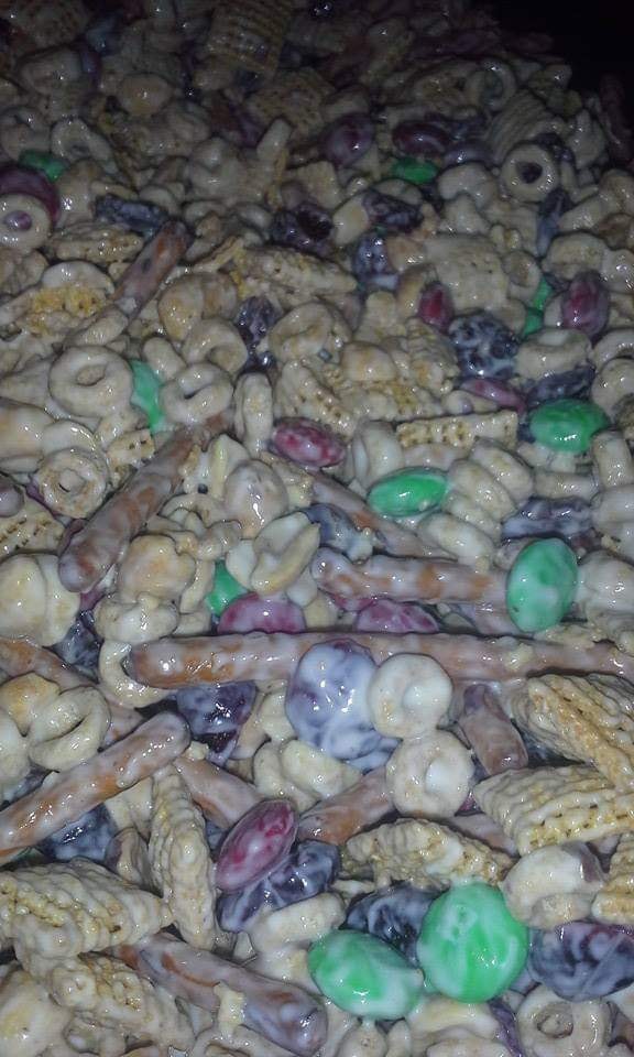 A close-up of Christmas Crack Snack Mix featuring Cheerios, Chex, pretzels, M&Ms, and white chocolate