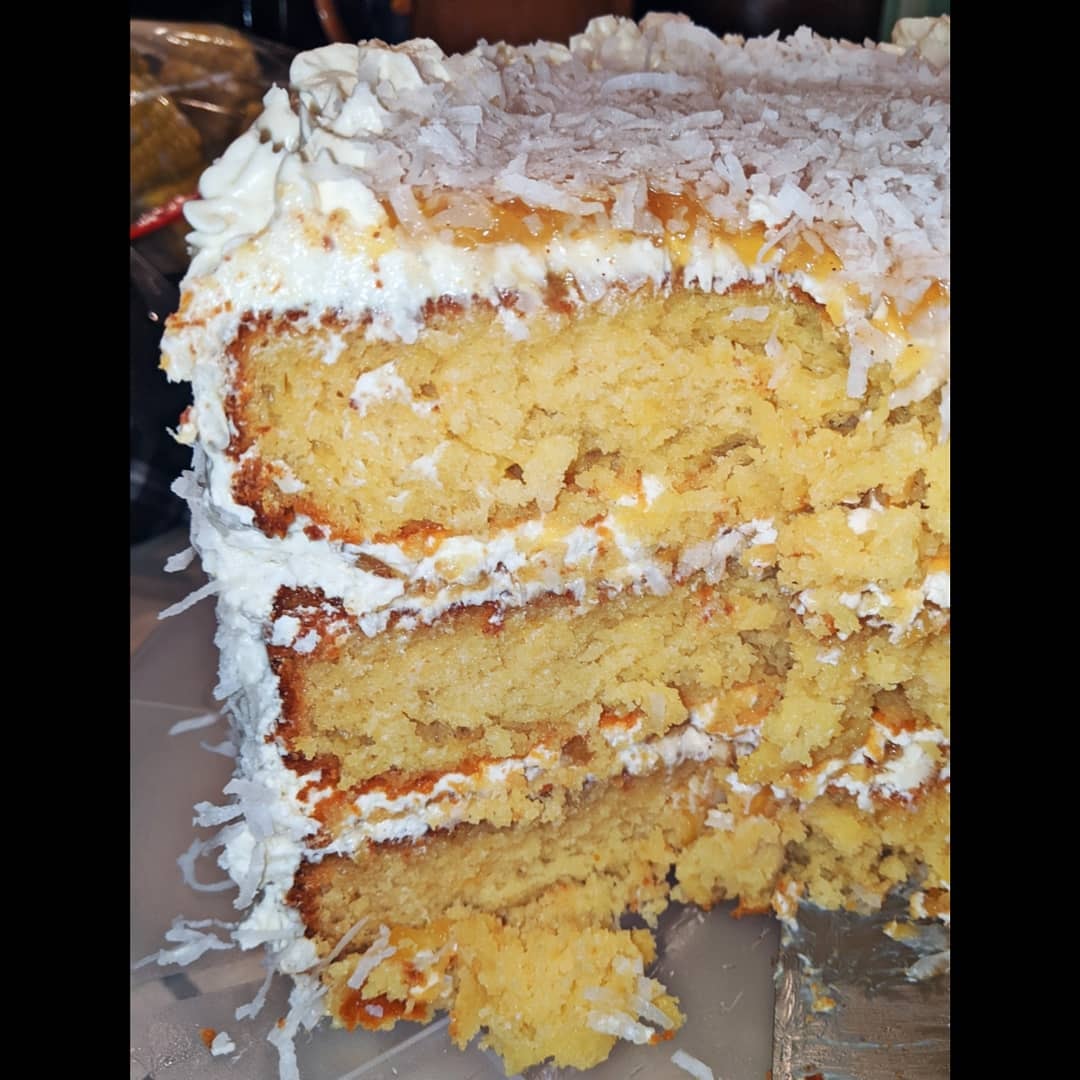 A slice of vanilla coconut cake with layers of cream cheese frosting and caramelized pineapple filling.