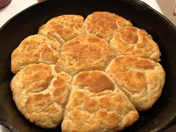 A batch of golden-brown buttermilk biscuits baked in a cast iron skillet, fluffy and ready to serve