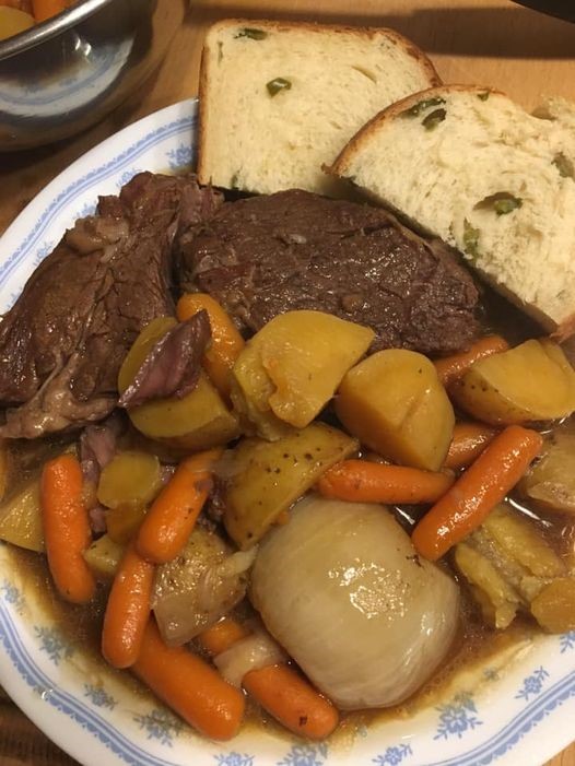 "A plate of tender Mississippi pot roast, baby carrots, potatoes, onions, and slices of jalapeño bread, perfect for a comforting family dinner.