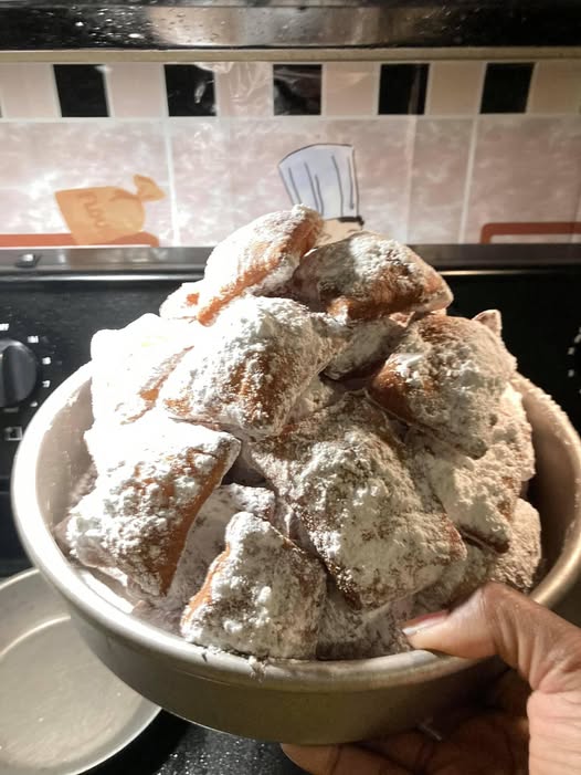 A bowl of homemade beignets dusted generously with powdered sugar, fresh from the fryer