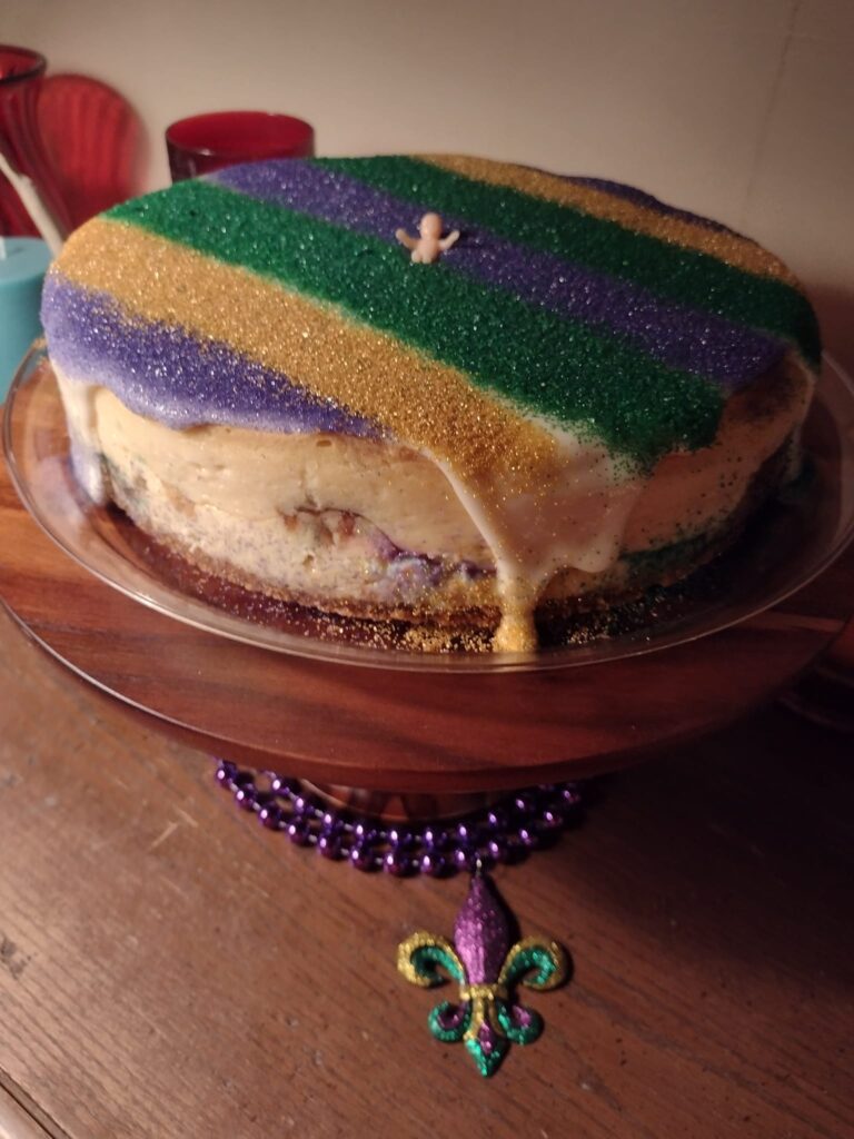 A beautifully decorated King Cake Cheesecake with traditional Mardi Gras colors.