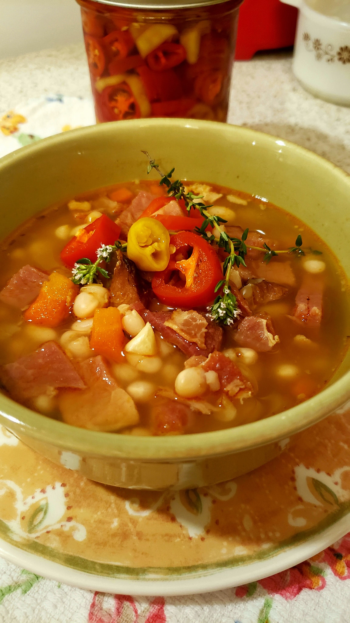 Steaming bowl of navy bean ham bone soup with pickled peppers and cornbread on a rustic wooden table