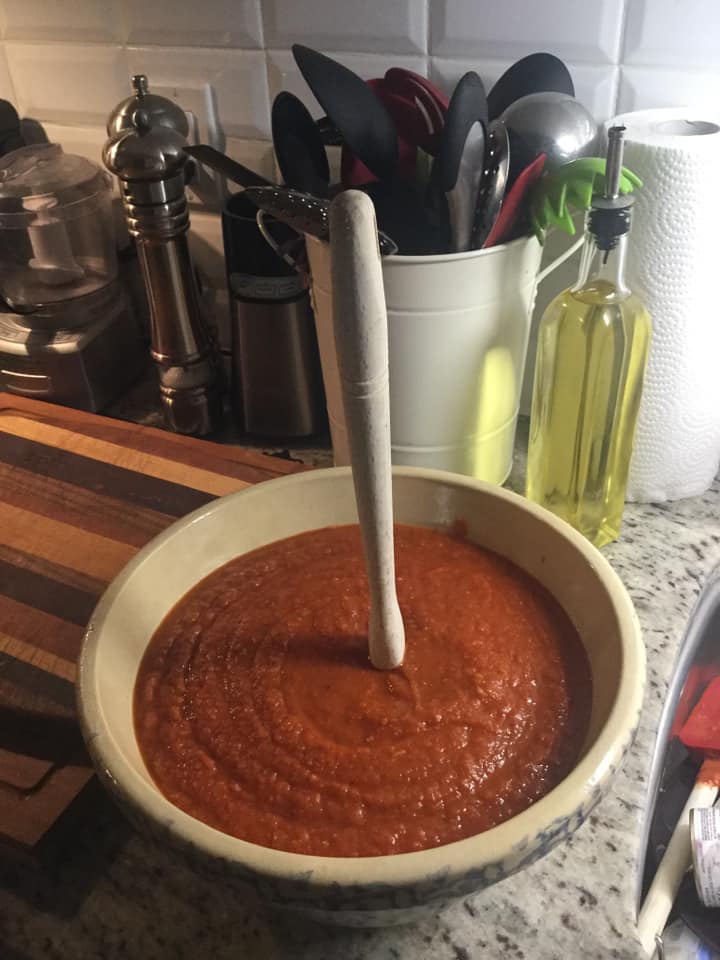 A thick, rich homemade pizza sauce in a rustic ceramic bowl with a wooden spoon standing upright in the center, showcasing its perfect consistency