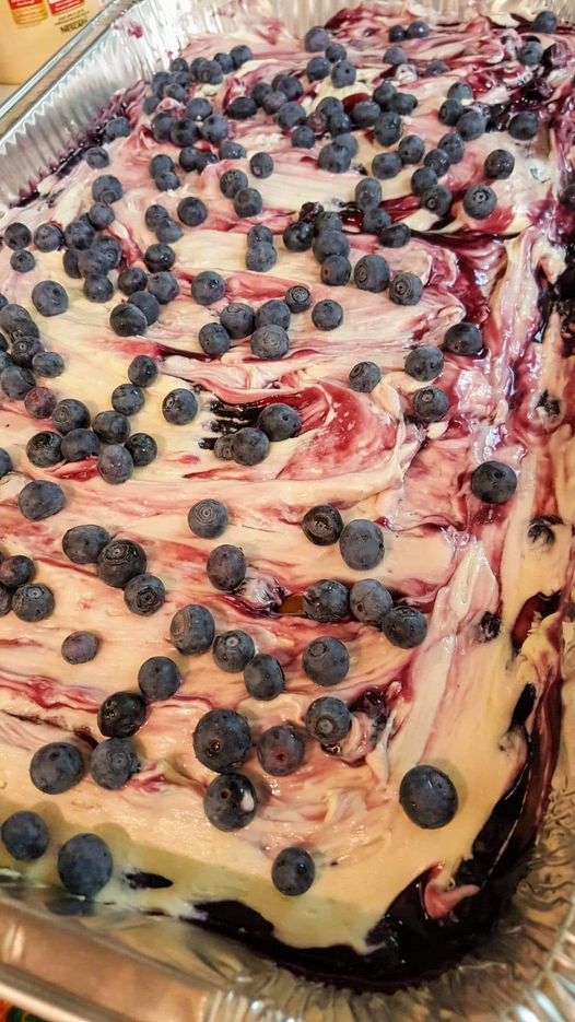 A freshly made blueberry cobbler cake with swirled cream cheese frosting and fresh blueberries on top.