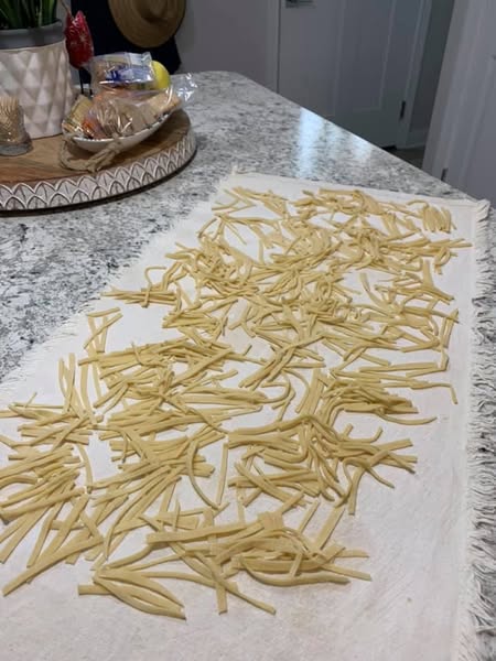 Freshly cut homemade egg noodles drying on a floured cloth before cooking