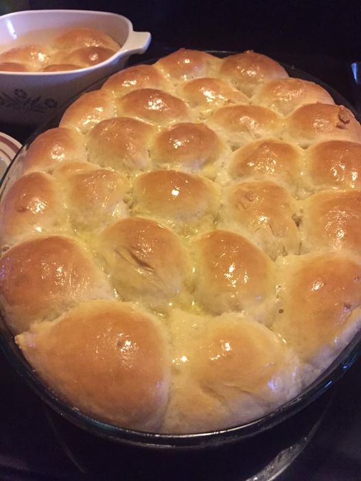 A pan of freshly baked golden-brown hot rolls, brushed with melted butter.
