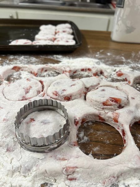 Strawberry biscuit dough rolled out on a floured surface with a biscuit cutter in use.