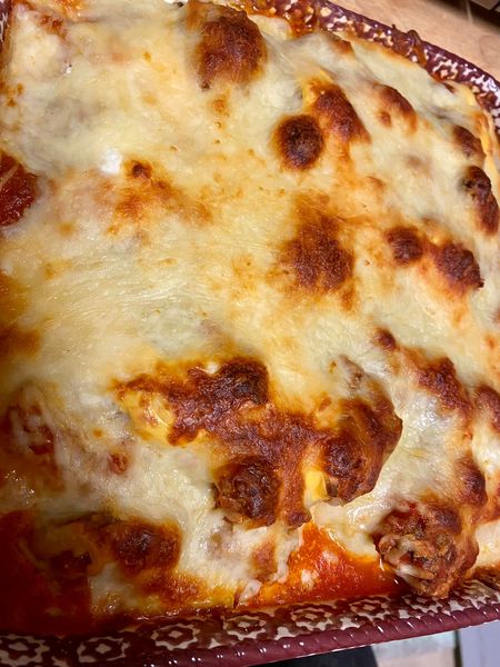 A close-up of a homemade baked pasta dish with melted cheese and a rich meat sauce. The pasta is cut open, revealing a flavorful filling.