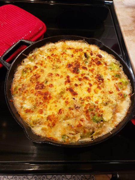A skillet filled with creamy Brussels sprouts topped with melted cheese and crispy bacon.