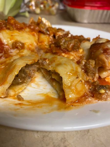 A serving of cheesy, meaty baked ravioli on a white plate, with a fork in the background. The dish is covered in tomato sauce and gooey melted cheese