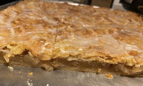 Close-up of a sliced apple slab pie showing the crispy crust, soft apple filling, and a drizzle of powdered sugar glaze