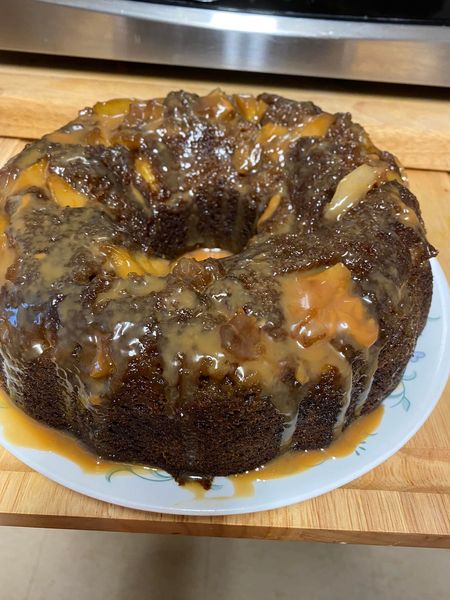 A rich caramel apple cake with a golden brown caramel drizzle, sitting on a white plate."