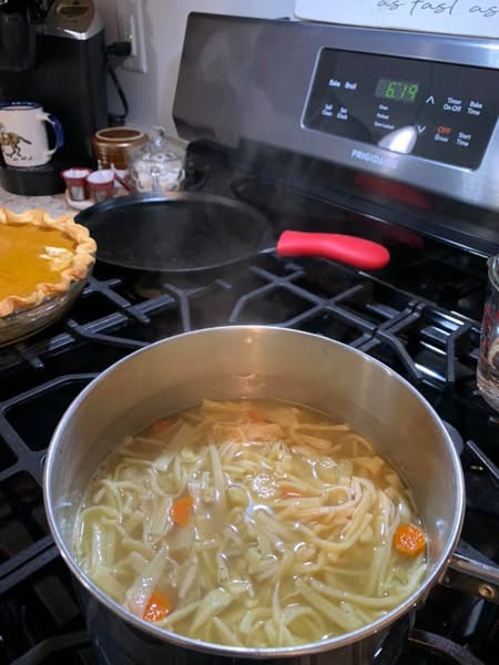 A steaming pot of homemade chicken noodle soup with fresh egg noodles, carrots, and celery simmering on the stove