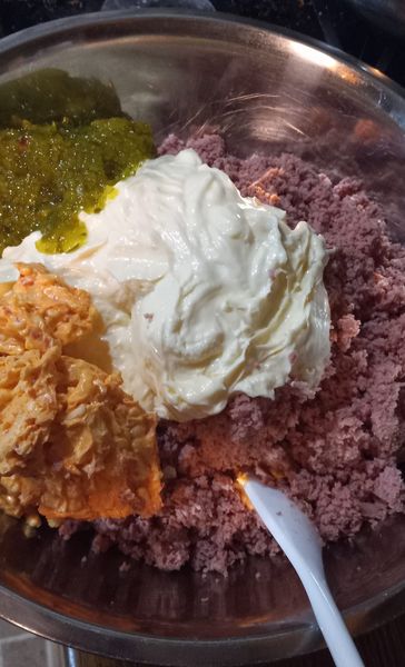 A bowl of bologna salad being mixed with mayo, pickle relish, and pimento spread.