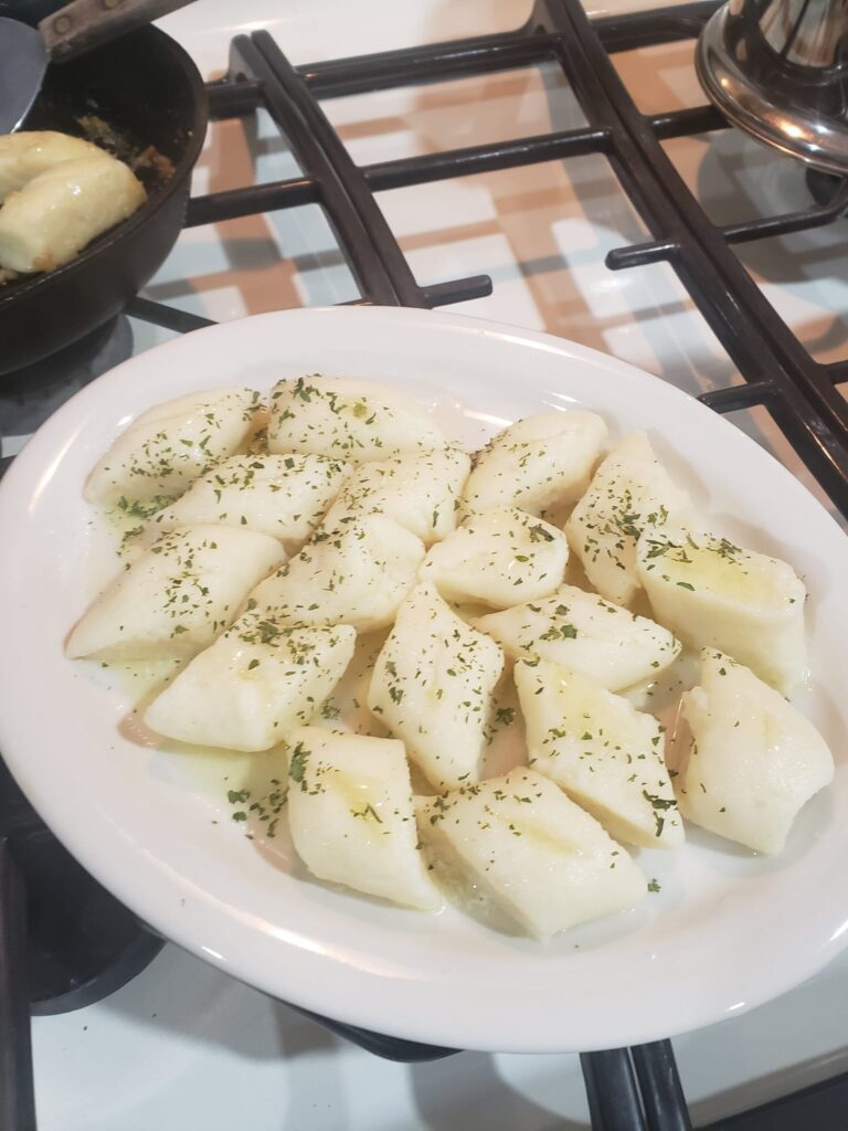 Polish Kopytka dumplings plated with melted butter and herbs, ready to serve