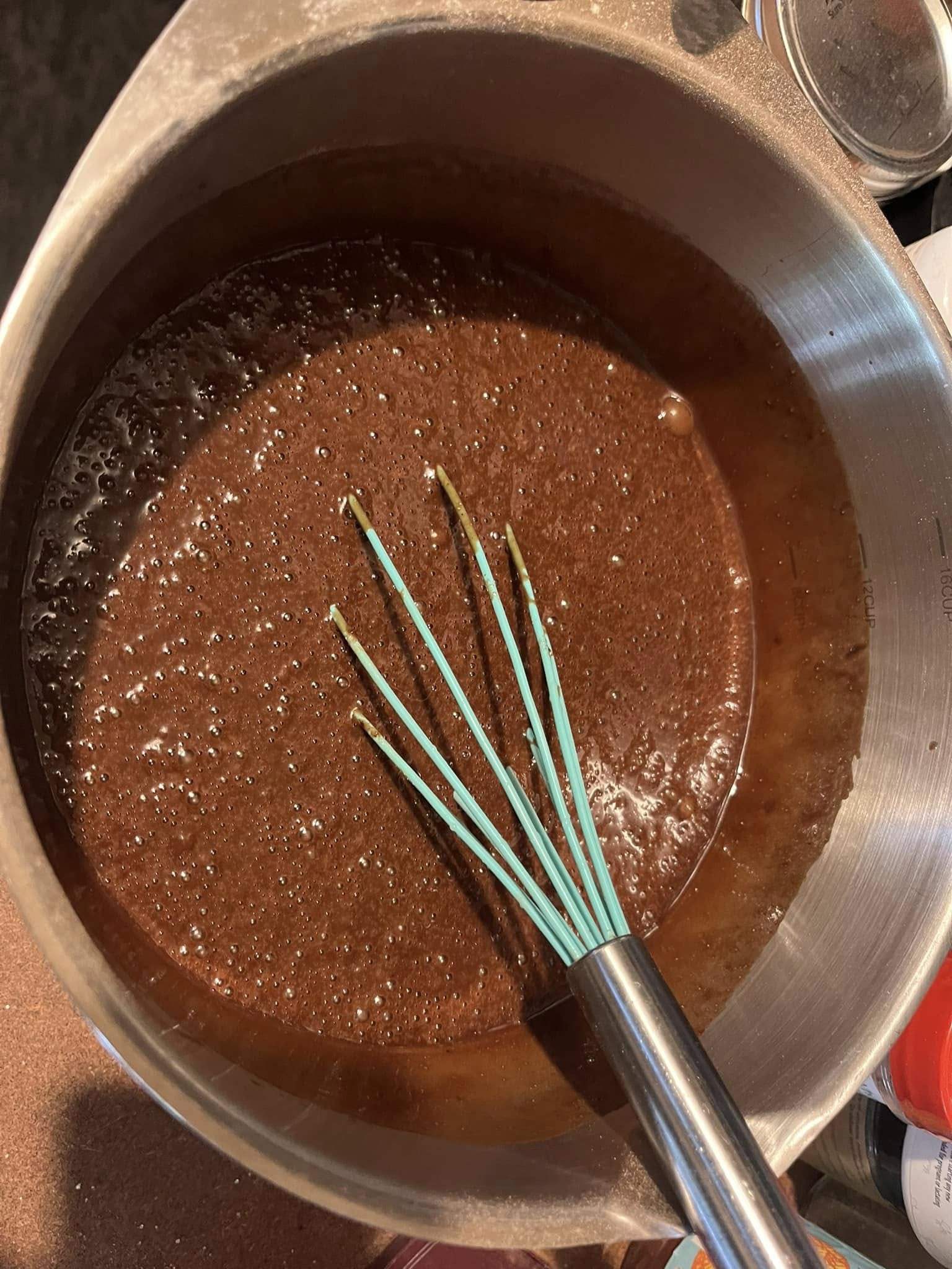 A metal mixing bowl with a whisk stirring a thin, chocolate cake batter.