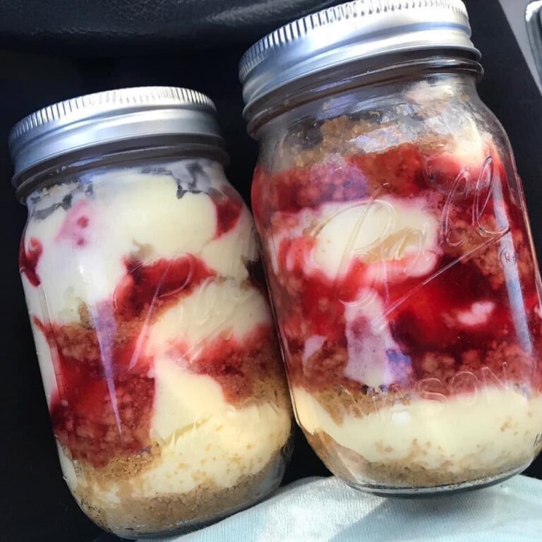 Two mason jars filled with luscious strawberry cheesecake, held in hand, displaying the perfect combination of textures and flavors.