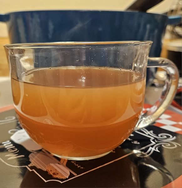 A clear glass cup filled with homemade apple cider, served warm with a rich golden hue.