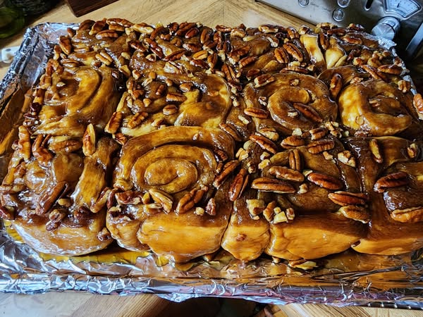 A caramel roll on a blue plate, topped with pecans and drizzled with sticky caramel sauce